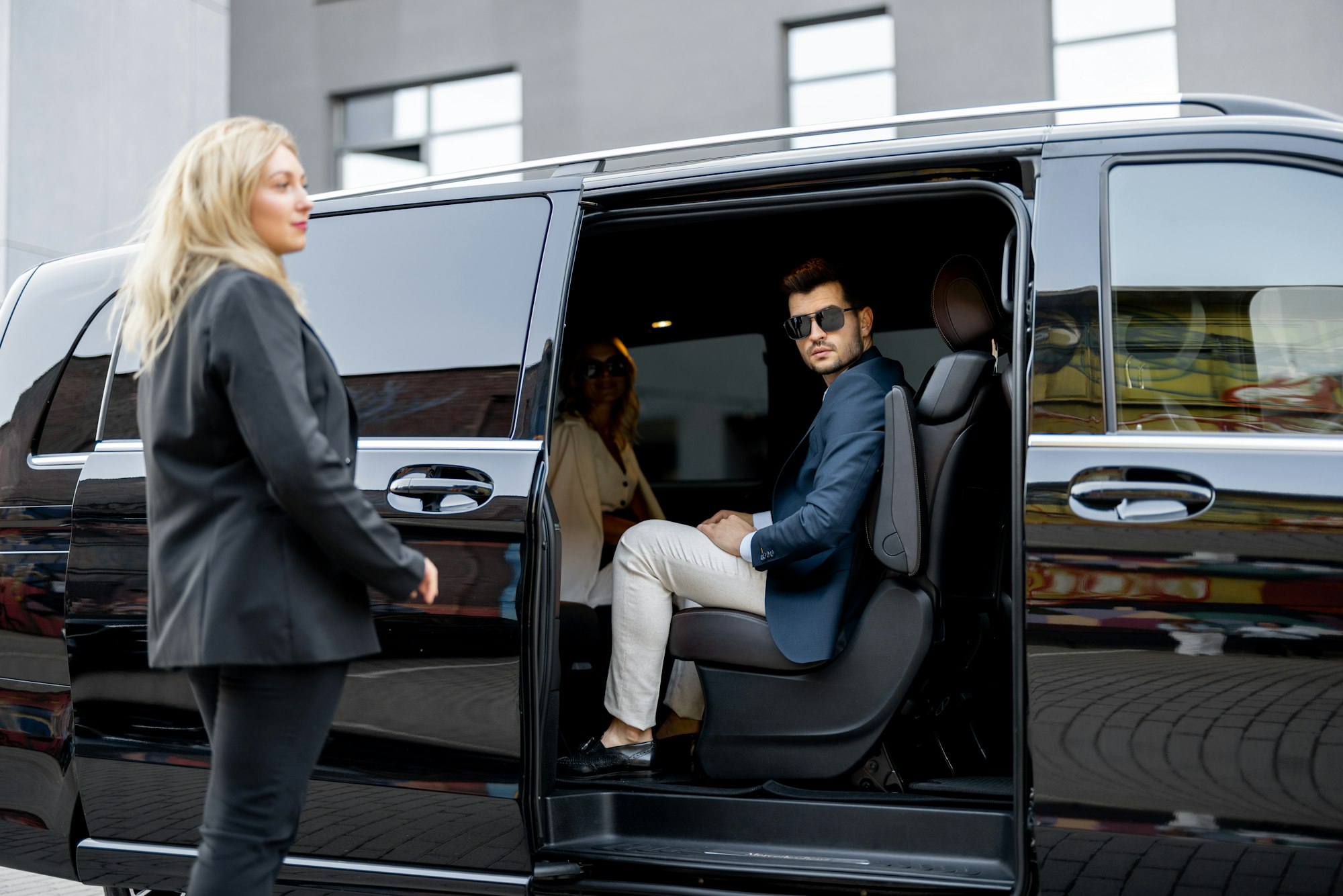 Female CEC Minicabs chauffeur helps business people to get out of a Minibus taxi